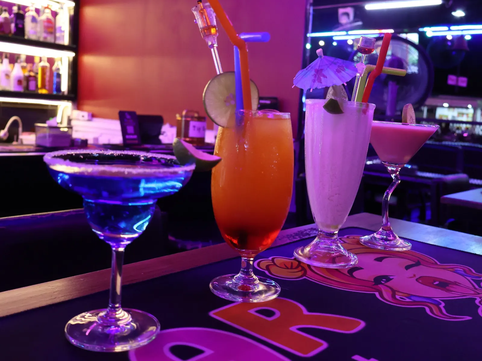 Four colorful cocktails lined up on the bar